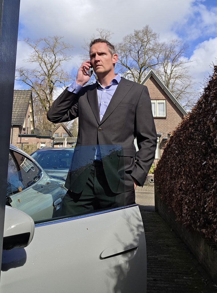 Rick Evers staat in pak bij een auto te bellen